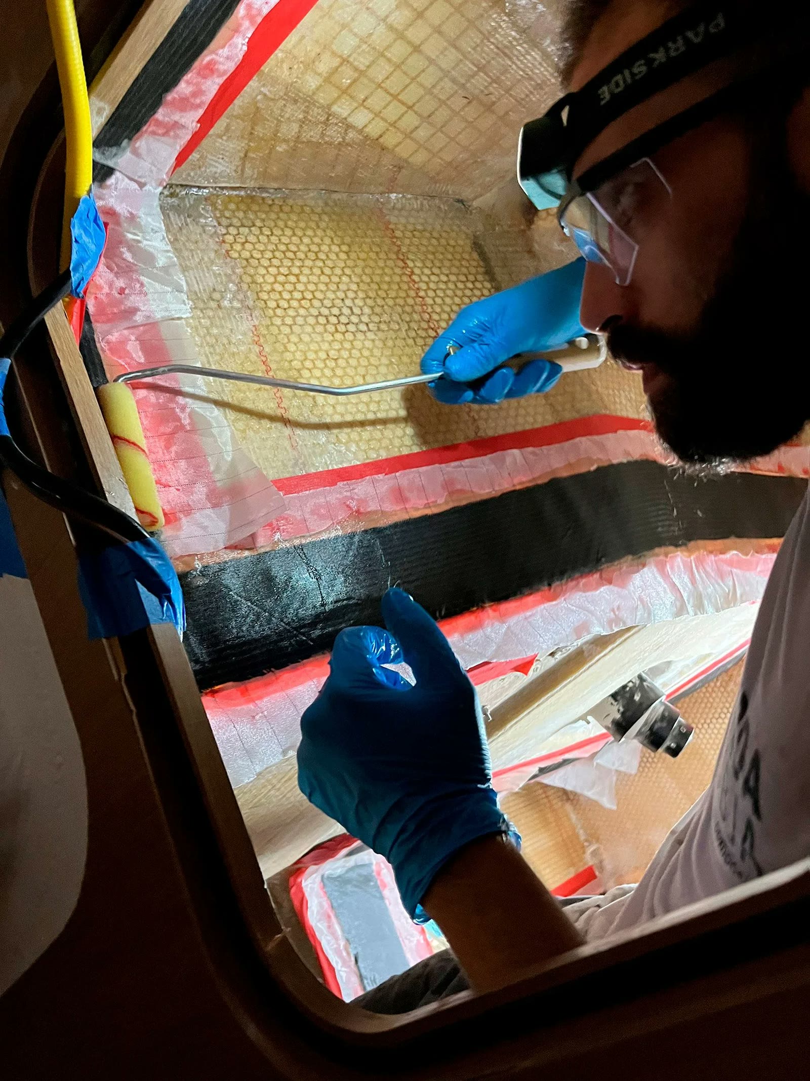 Hands in blue gloves rolling resin into carbon fabric on a hull mould in the Assemini workshop