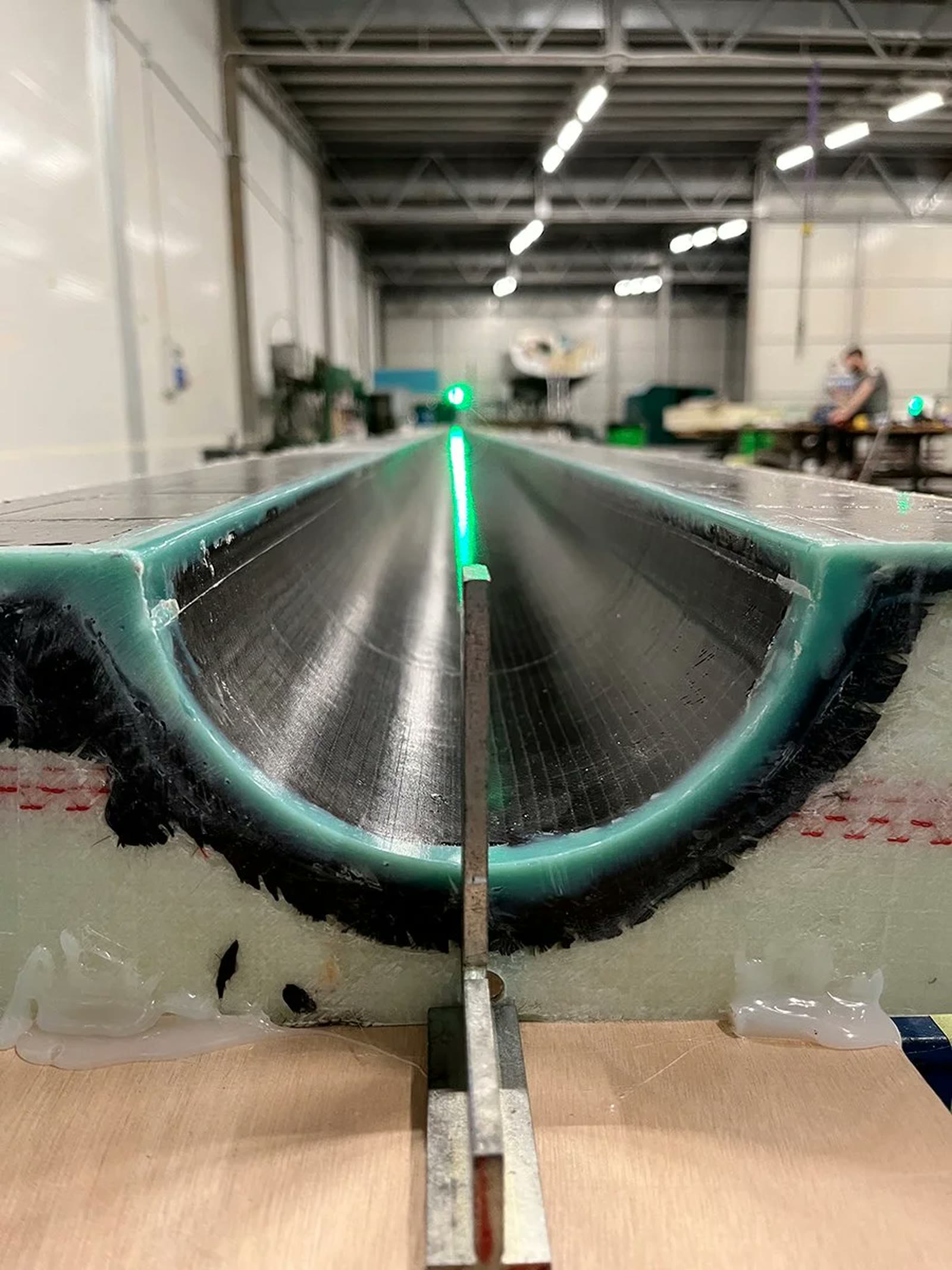 A carbon fibre hull section on the bench in the Assemini workshop, a laser line along its axis