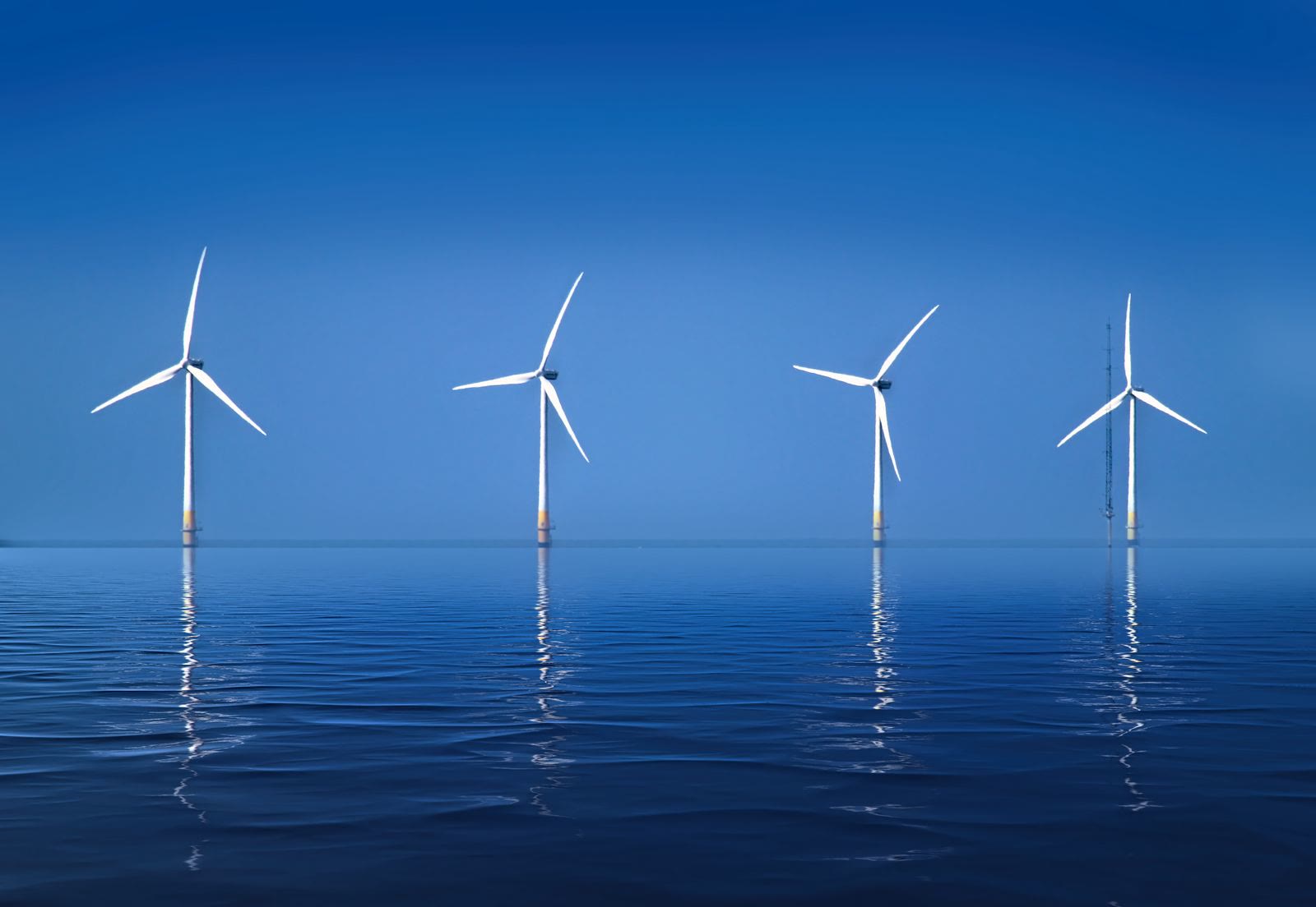 A row of offshore wind turbines reflected on a calm sea