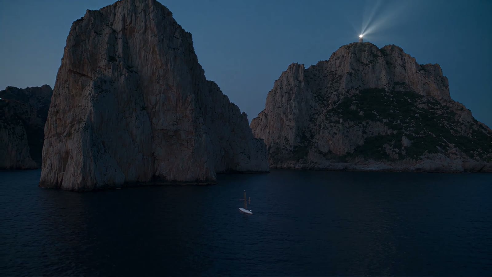 Two rocky sea stacks at night with a lighthouse beam sweeping across, a small hull on the dark water below